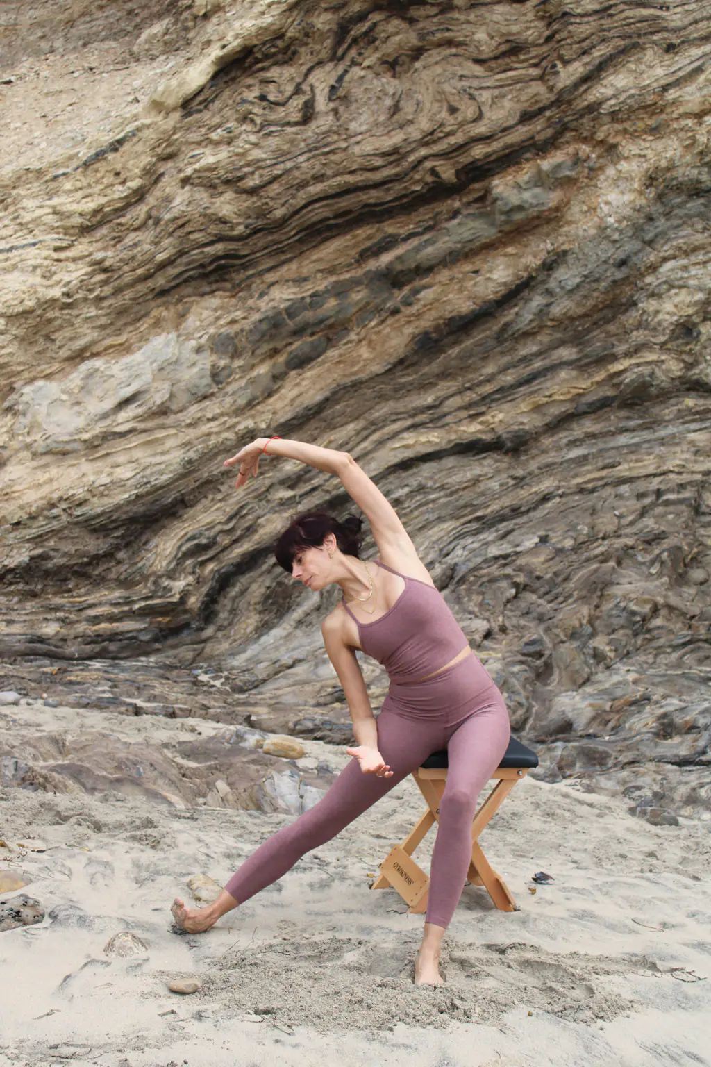 Arpi in a flowing side stretch on a stool against a sandstone cliff